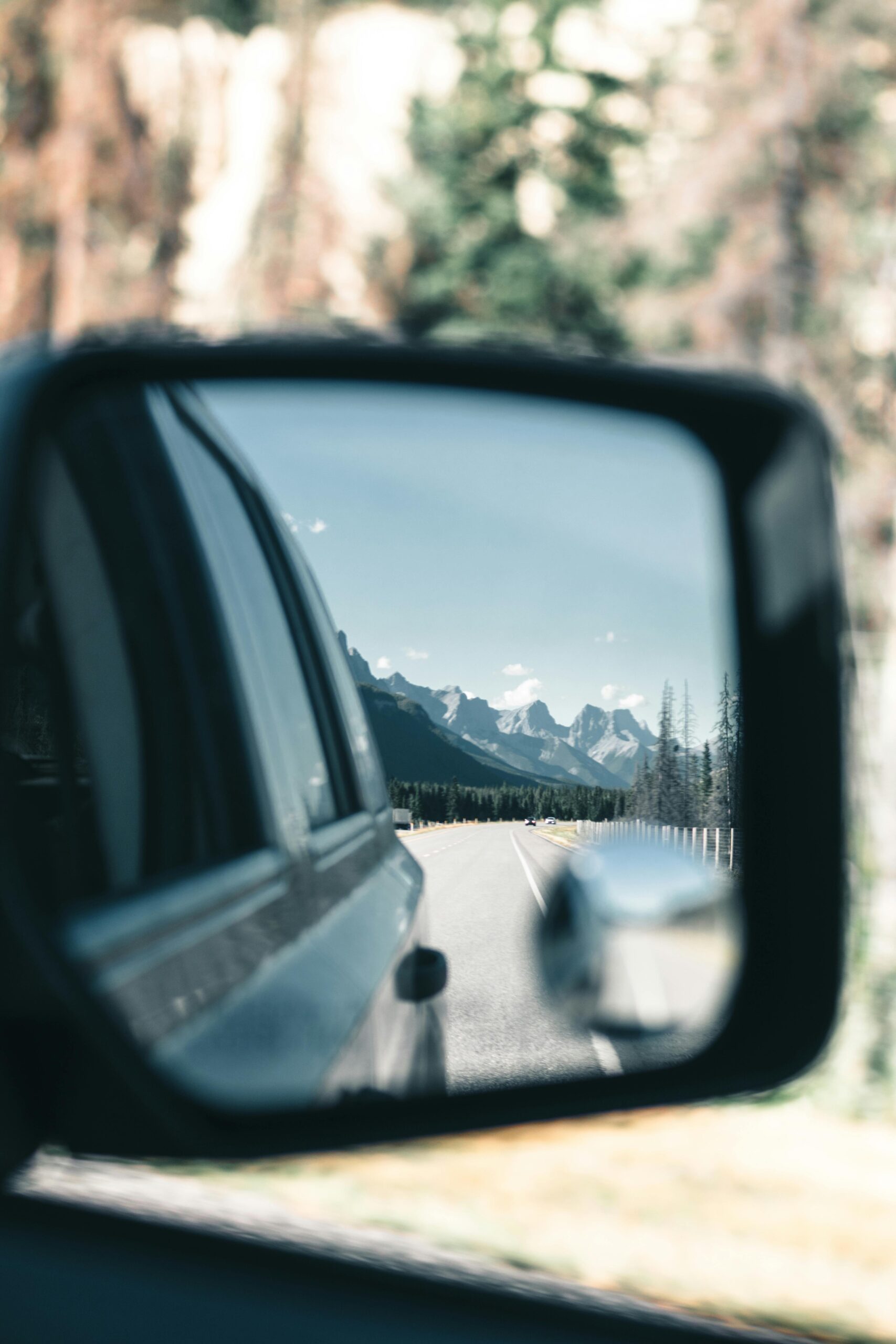 Reflection of a mountain landscape in a car side mirror during a road trip.
